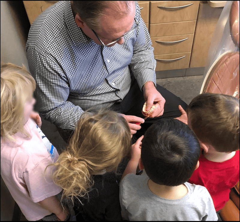 Dr. Rogers, surrounded by children, showing them a dental tooth model